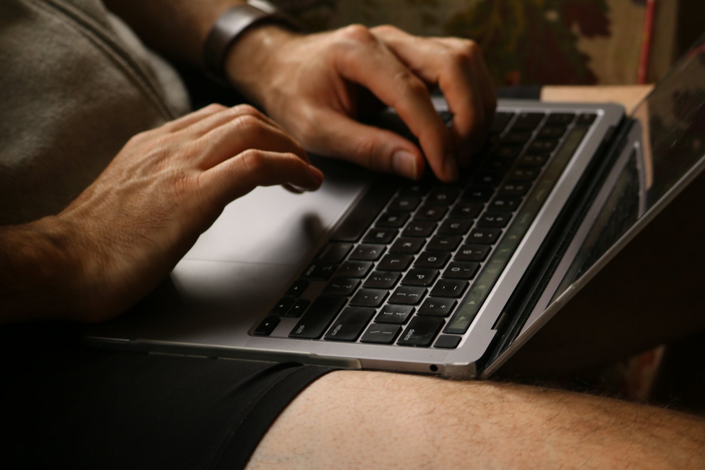 Hands typing on a silver laptop resting on a lap.