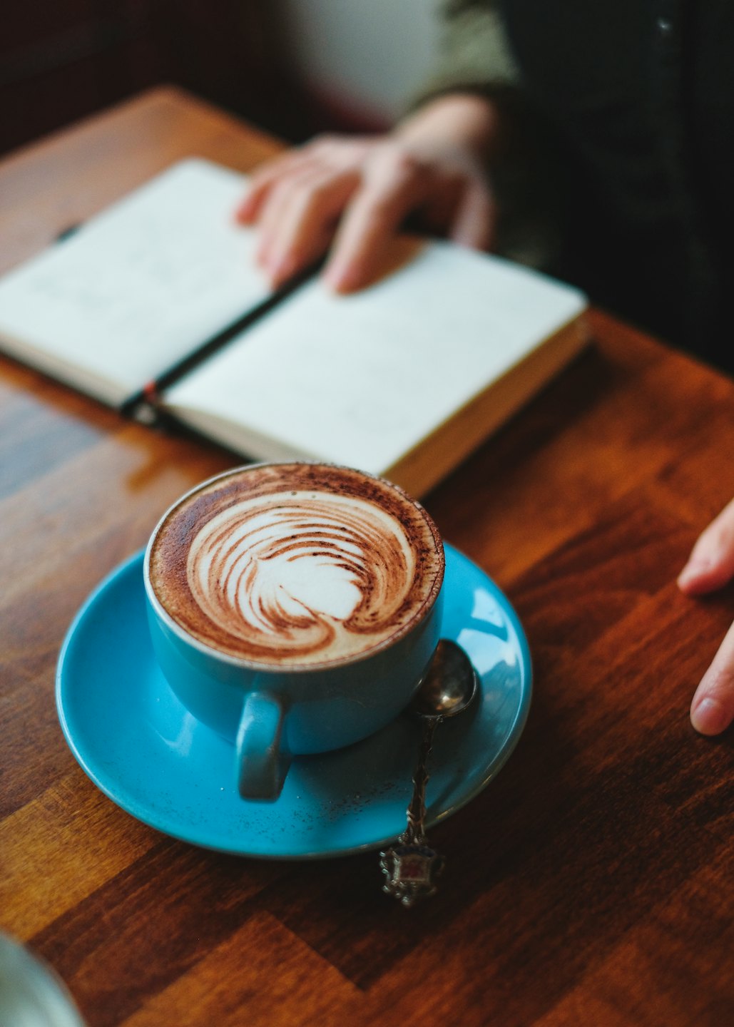 Hands near a blank notebook and blue coffee cup.